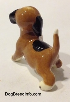 The back left side of a miniature Beagle figurine in a standing pose with its paw up. The figurine has its tail in the air.