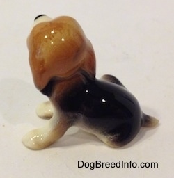 The back of a black, brown and white Beagle puppy figurine. The figurine has a short tail.