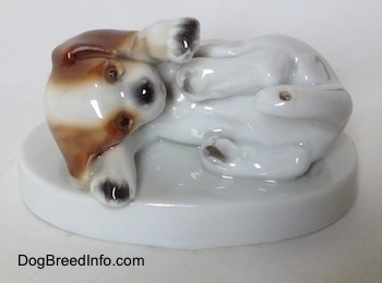 A white with brown and black Beagle puppy figurine. The puppy in the figurine is laying on its right side.