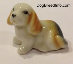 The left side of a bone china white with tan and black tiny Beagle puppy figurine. The figurine has a simple face.