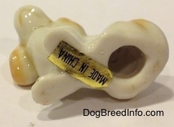 The underside of a bone china white with tan and black tiny Beagle puppy figurine. There is a hole and a sticker that reads - MADE IN CHINA - on the underside of the figurine.