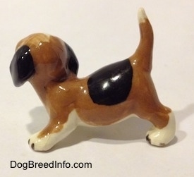 The left side of a brown, black and white miniature Beagle in a crouching pose. The figurine has a big black spot on its back.