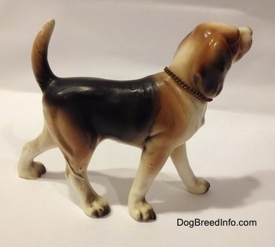 The right side of a black, brown and white ceramic Beagle figurine with a chain ID collar that reads "Beagle". The figurine has very great leg details.