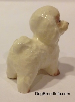 The back right side of a white with tan miniature Bichon Frise dog figurine. The figurine has a tail that is indistinguishable from its body.