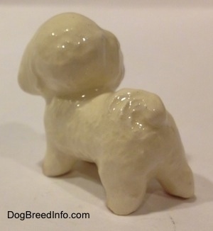 The back left side of a white with tan miniature Bichon Frise dog figurine. The figurine is glossy.