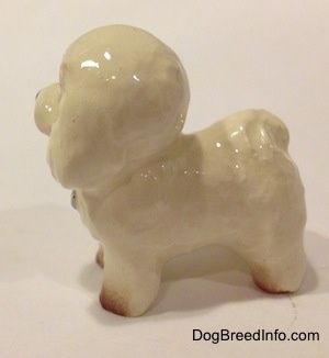 The right side of a white with tan miniature Bichon Frise dog figurine. The dogs tail is curled up over its back.