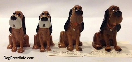 A line up of four Hagen-Renaker Bloodhound figurines. The figurines has very cartoon-y details with big black noses and black eyes.