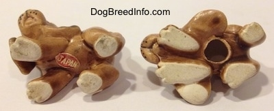 The underside of two Vintage miniature ceramic Bloodhound figurines. There is a sticker with the word -JAPAN - on the underside of the left most figurine and the one on the right has a hole on its underside.