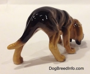 The back right side of a brown and black Hagen Renaker Miniature Bloodhound figurine. Its back legs are spread wide apart.