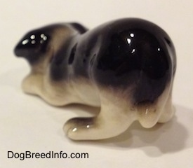 The back left side of a Hagen-Renaker miniature black with white Border Collie puppy figurine. Its hard to tell the difference between the tail of the figurine and its body.