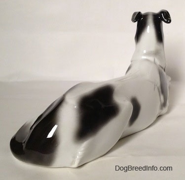 The back right side of a white with black vintage Borzoi figurine that is laying down. The figurine lacks fine details on the body.