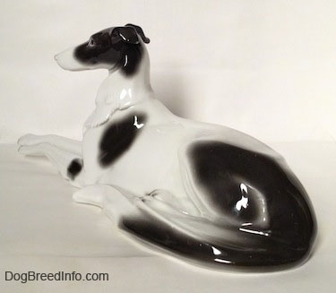 The back left side of a white with black vintage Borzoi figurine that is laying down.