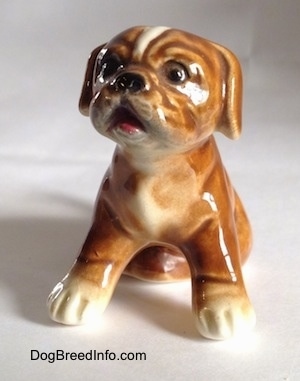 A brown with white Boxer puppy figurine that is in a sitting pose. The figurine is very glossy.
