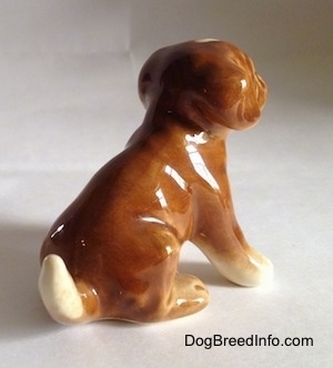 The back right side of a brown with white Boxer puppy figurine that is in a sitting pose. The figurine lacks fine paw details.