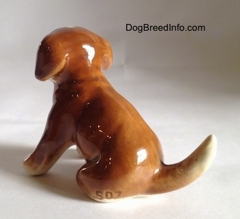 The back left side of a brown with white Boxer puppy figurine that is in a sitting pose. Engraved on the hind leg of the figurine is te number - 507.