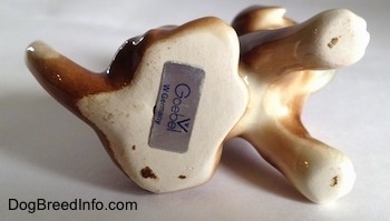 The underside of a brown with white Boxer puppy figurine that is in a sitting pose. There is a sticker at the bottom with the logo for Goebel W.Germany on it.
