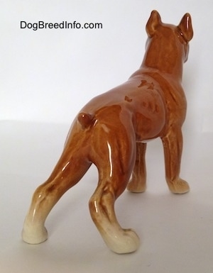 The back right side of a porcelain brown Boxer dog figurine. The figurine has a short tail.