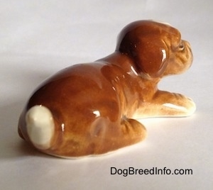 The back right side of a brown with white Boxer puppy figurine. The figurine has an arched up tail.