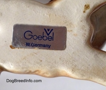 The underside of a brown with white Boxer puppy figurine. The figurine has a sticker with the Goebel W.Germany logo on it.