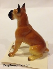 The left side of a tan with black and white Boxer papa figurine. The tips of the figurines paws are black.