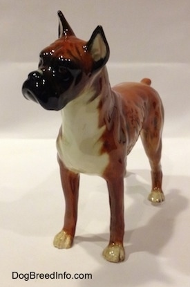 The front left side of a 1970s brown with black and white Boxer dog figurine. The figurine has fine paw details.