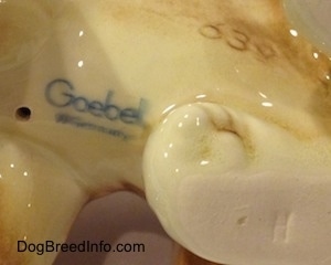 Close up - The underside of a brown with white Boxer puppy figurine. On the underside the figurine has a Goebel W.Germany logo on the bottom.