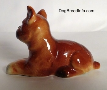The left side of a brown with white and black Boxer puppy figurine. The figurine has a short tail.
