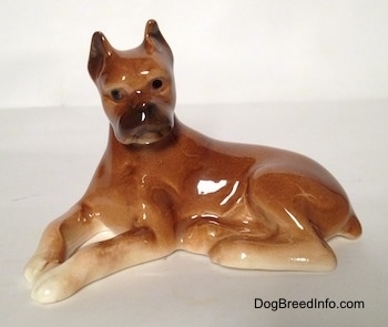 The left side of a brown with tan Boxer dog figurine in a laying down pose. The figurine has black circles for eyes.