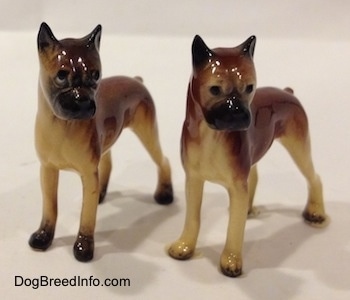 The front left side of two different color variations of the miniature Boxer Mama figurine. The figurines both have black circles for eyes.