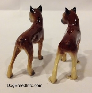 The back right side of two different color variations of the miniature Boxer mama figurine. The figurines have black ears.