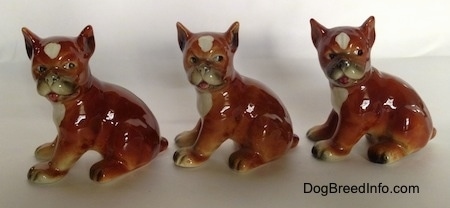 The left side of three brown with white and black Boxer puppy figurines that are slightly different.