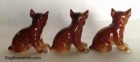 The right side of three brown with white and black Boxer puppy figurines. The figurines have detailed paws.