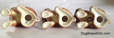 The underside of three brown with white and black Boxer puppy figurines. There is a hole in the bottom of each figurine and under that is the Goebel W. Germany logo.