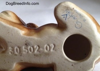 Close up - The underside of a Boxer puppy figurine. On the bottom there is a hole, above it is a Goebel W. Germany logo and to the left of the hole is the engraved number - 30502-02.
