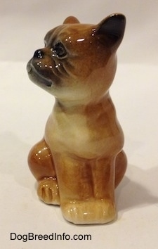 A brown with white Boxer puppy figurine that is in a sitting pose. The paws of the figurine are attached together.