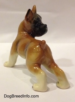 The back left side of a brown with white and black porcelain Boxer dog figurine. The figurine is very glossy.