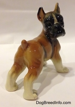 The back right side of a brown with white and black porcelain Boxer dog figurine. The figurine has fine details.