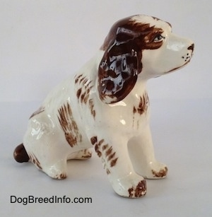 The right side of a brown and white ceramic Brittany Spaniel that is in a sitting pose. The ears of the figurine has great details.