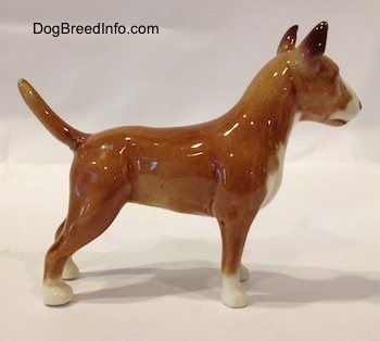 The right side of a brown with white Bull Terrier figurine. The figurine is glossy. The dogs body is tan and its paws are white.