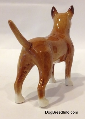 The back right side of a brown with white Bull Terrier figurine. The figurines tail is arched up.