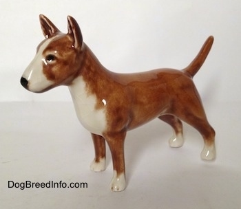 The left side of a brown with white Bull Terrier figurine. The figurine has circles for eyes.