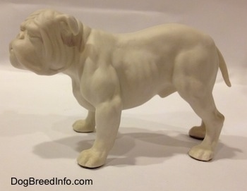 The left side of a white bisque porcelain Bulldog figurine. The figurine has a medium length tail.
