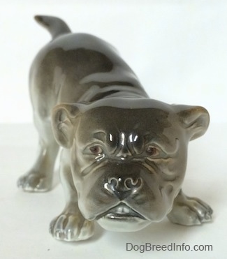 A gray and white Bulldog figurine in a play bow pose. The figurine has a slightly detailed face.