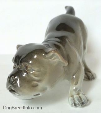 The front left side of a gray and white Bulldog figurine in a play bow pose. The paws of the figurine have fine details.