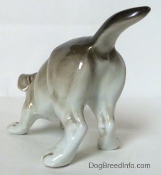 The back left side of a gray and white Bulldog figurine in a play bow pose. The figurine has white paws.
