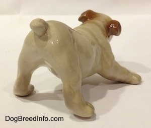 The back right side of a tan with brown Bulldog puppy figurine that is in a play bow pose. The tail of the figurine is easy to differentiate from the body.