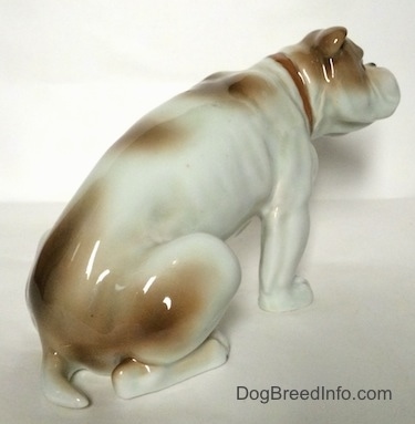 The back right side of a white with brown Bulldog figurine in a sitting pose. The figurine has very detailed paws.