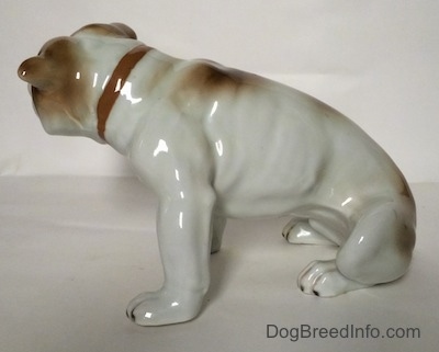 The left side of a white with brown Bulldog figurine in a sitting pose. The figurine has great details on its body and paws.