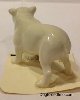 The back left side of a white miniature Bulldog figurine. It is hard to differentiate the tail from the body.