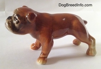The left side of a brown Bulldog figurine. The tail of the figurine is short and it is sticking out.